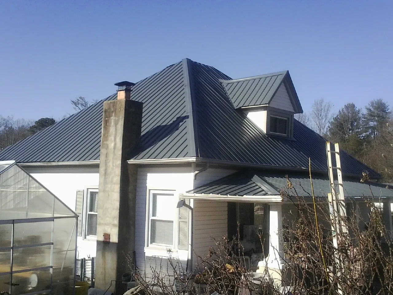 Dark blue standing seam metal roof on a white farmhouse with dormer — Slate & Tile Roof Repair by Roofing Brothers in Doucette