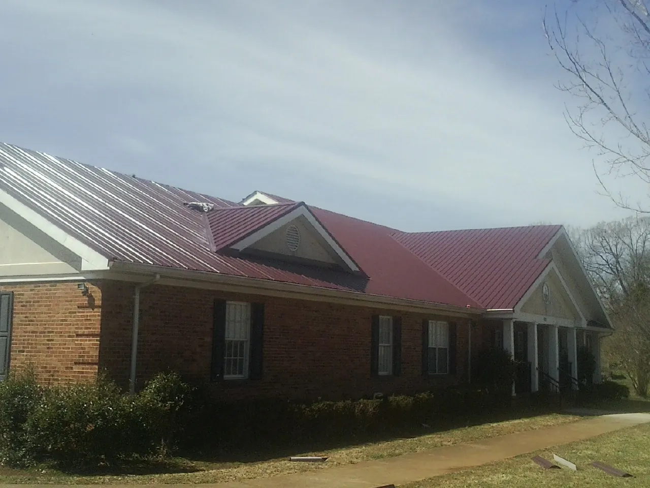 Red metal roof with gabled entries on a long brick building, from a Hail Damage Roof Repair job in Doucette