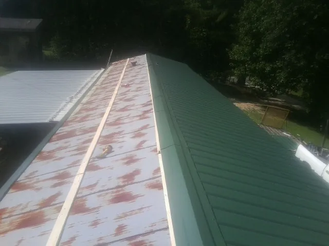Old rusted panels beside newly installed green metal roofing — Wind Damage Roof Repair by Roofing Brothers in Doucette