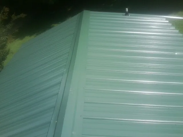 New green metal panels meeting at the ridge of a roof — Flat Roof Repair work by our crew in Doucette