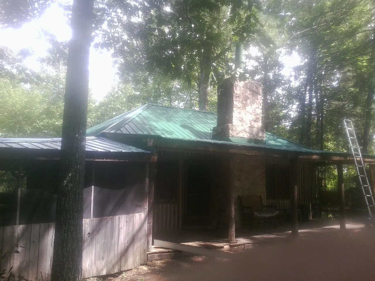 Green metal roof and stone chimney above a log cabin porch in Doucette