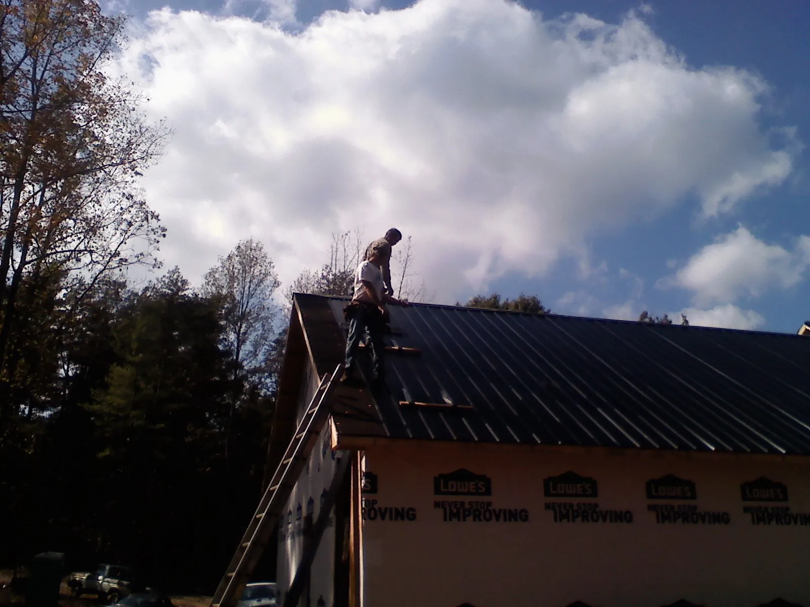 Roofer fastening dark metal panels high against a cloudy sky, from a Roof Inspection job in Doucette