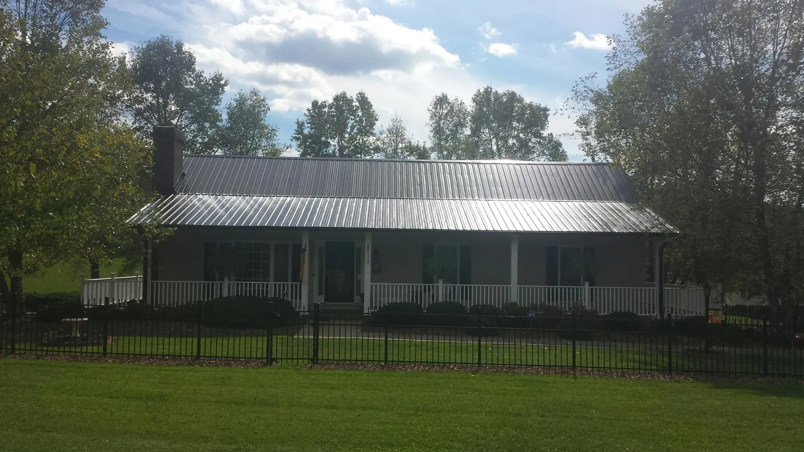Gray metal roof on a brick ranch with a full width front porch — Gutter Guard Installation work by our crew in Doucette