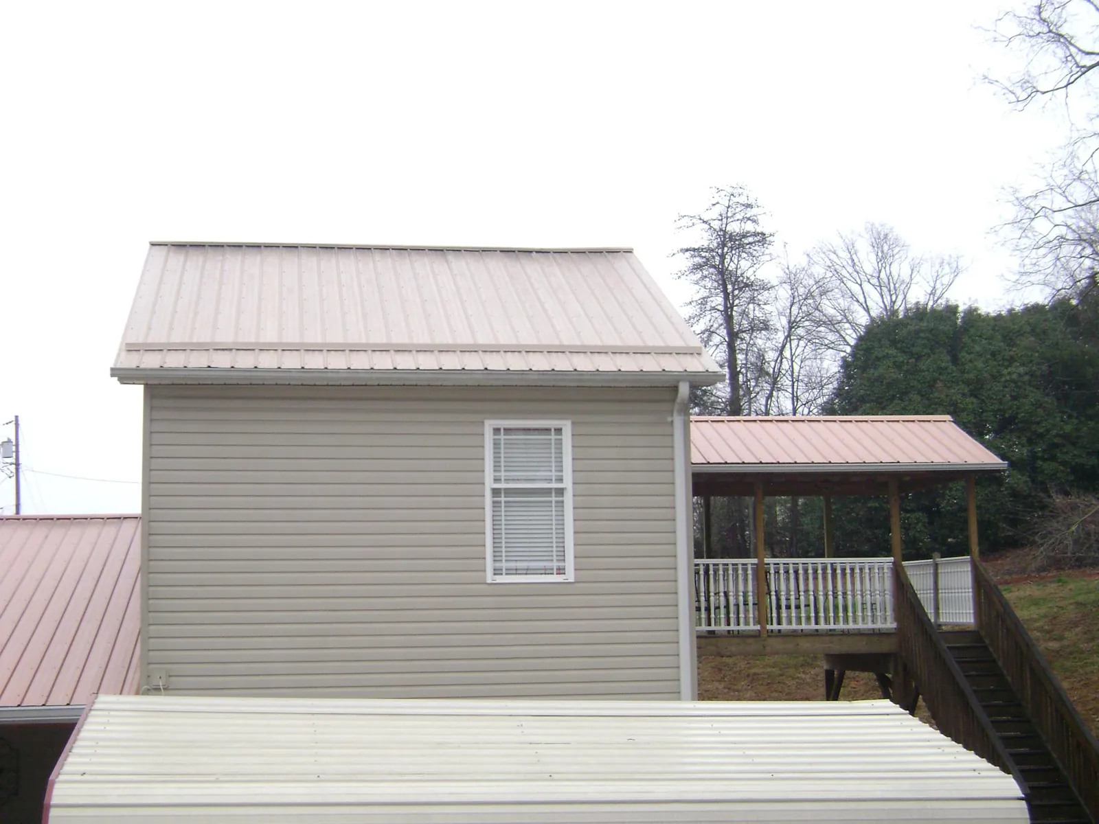 Tan metal roofs on a two story addition and attached porch, from a Roof Replacement job in Doucette